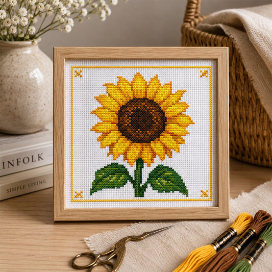 Sunflower cross stitch pattern featuring a bright yellow sunflower with green leaves and a decorative yellow stitched border, displayed as framed wall art.