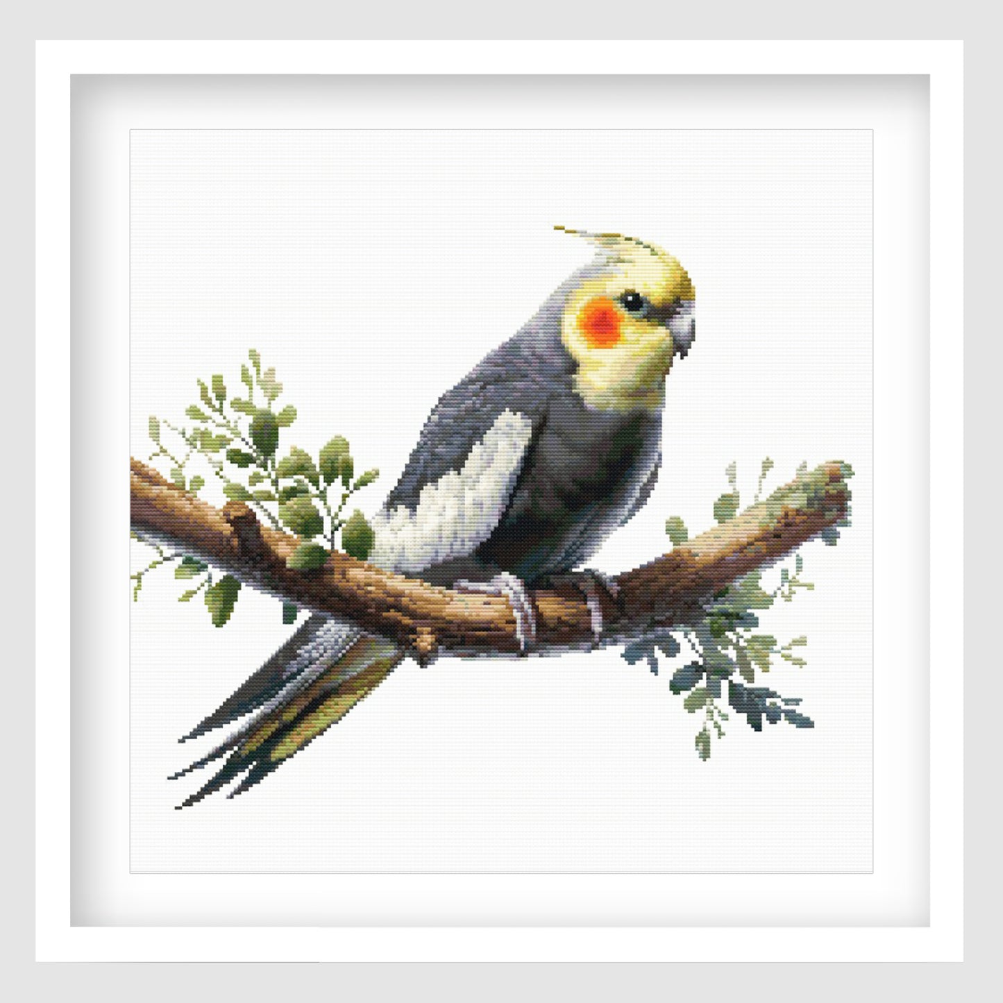 Cockatiel cross stitch pattern featuring a grey bird with yellow face and orange cheek markings, perched on a branch with soft green foliage.