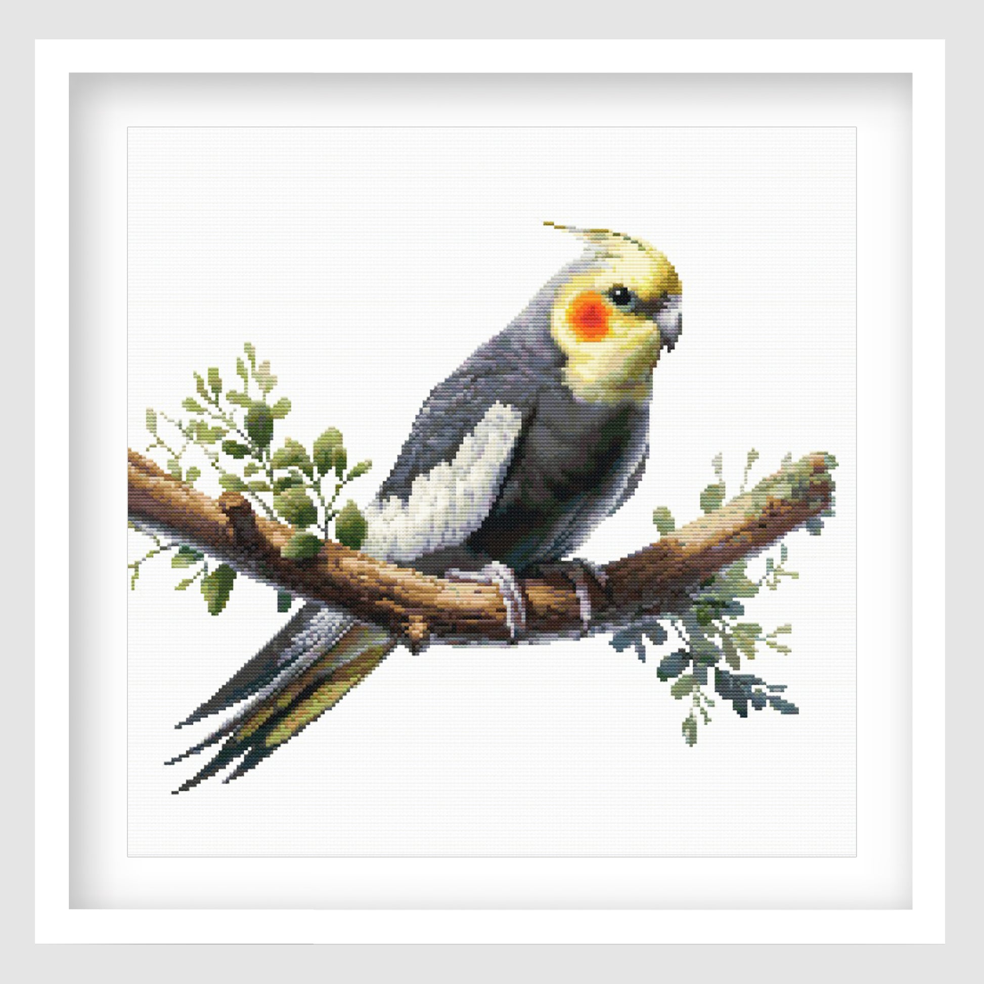 Cockatiel cross stitch pattern featuring a grey bird with yellow face and orange cheek markings, perched on a branch with soft green foliage.