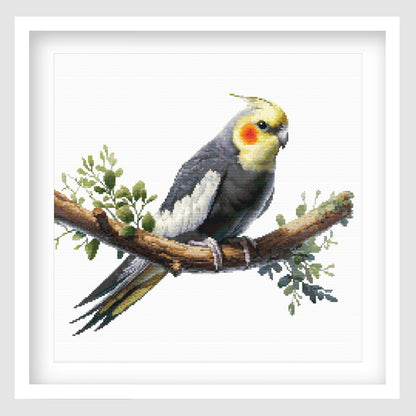 Cockatiel cross stitch pattern featuring a grey bird with yellow face and orange cheek markings, perched on a branch with soft green foliage.