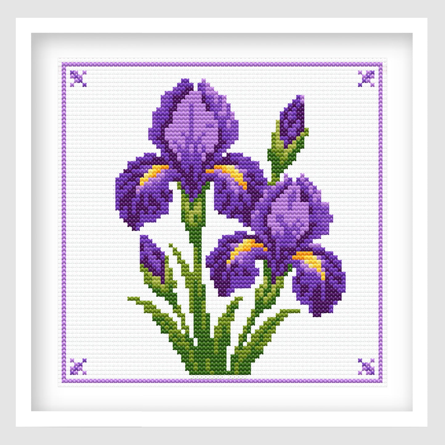 Cross-stitch-style artwork of several purple irises with green stems and leaves, accented with small yellow-orange details. The flowers are arranged in a bouquet on a white background, surrounded by a delicate purple stitched border with decorative corner motifs.