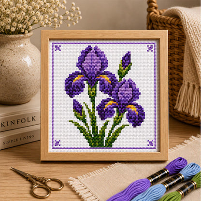 Framed purple iris cross stitch pattern displayed in a cosy home setting