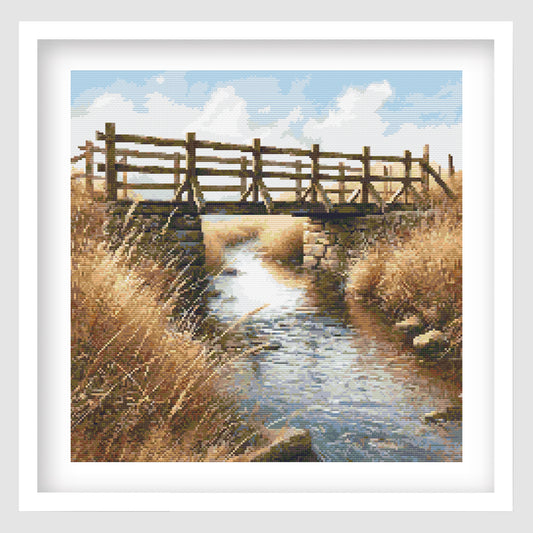 Wooden bridge over a stream with tall grasses and a blue sky.