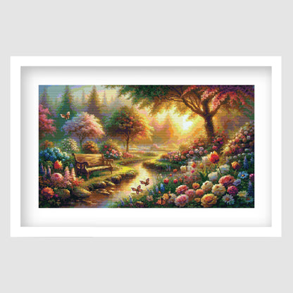 Sunrise garden cross stitch pattern featuring a glowing stream, wooden bench, butterflies and colourful flowers in a peaceful woodland landscape.