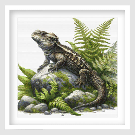 Tuatara cross stitch pattern featuring a detailed reptile resting on mossy rocks, surrounded by green ferns and natural forest foliage.