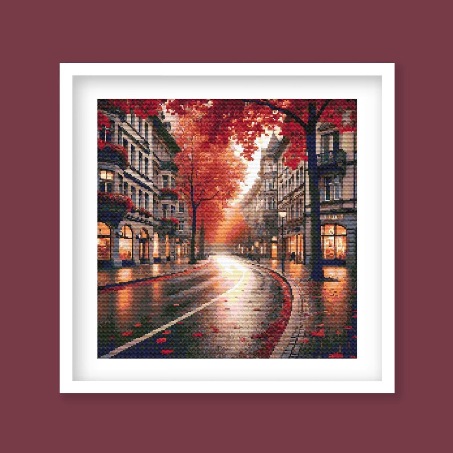 Autumn Cityscape Cross Stitch Pattern displayed as framed wall art with a glowing autumn street, red trees, city buildings, and warm seasonal detail.