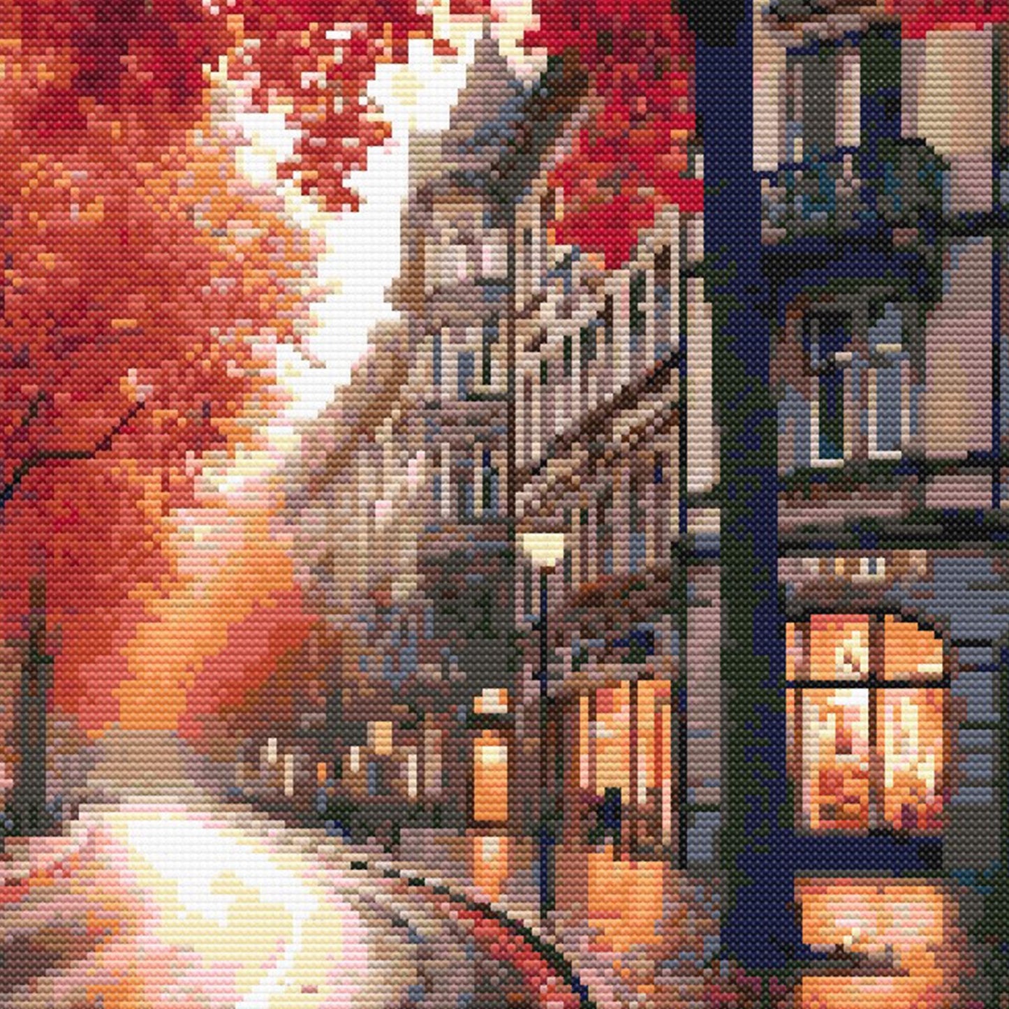 Close-up of Autumn Cityscape Cross Stitch Pattern showing a glowing city street, red autumn foliage, building detail, and visible counted cross stitch texture.