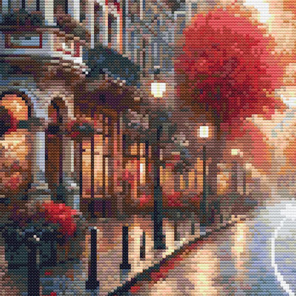Close-up of Autumn Cityscape Cross Stitch Pattern showing a glowing city street, red autumn foliage, building detail, and visible counted cross stitch texture.
