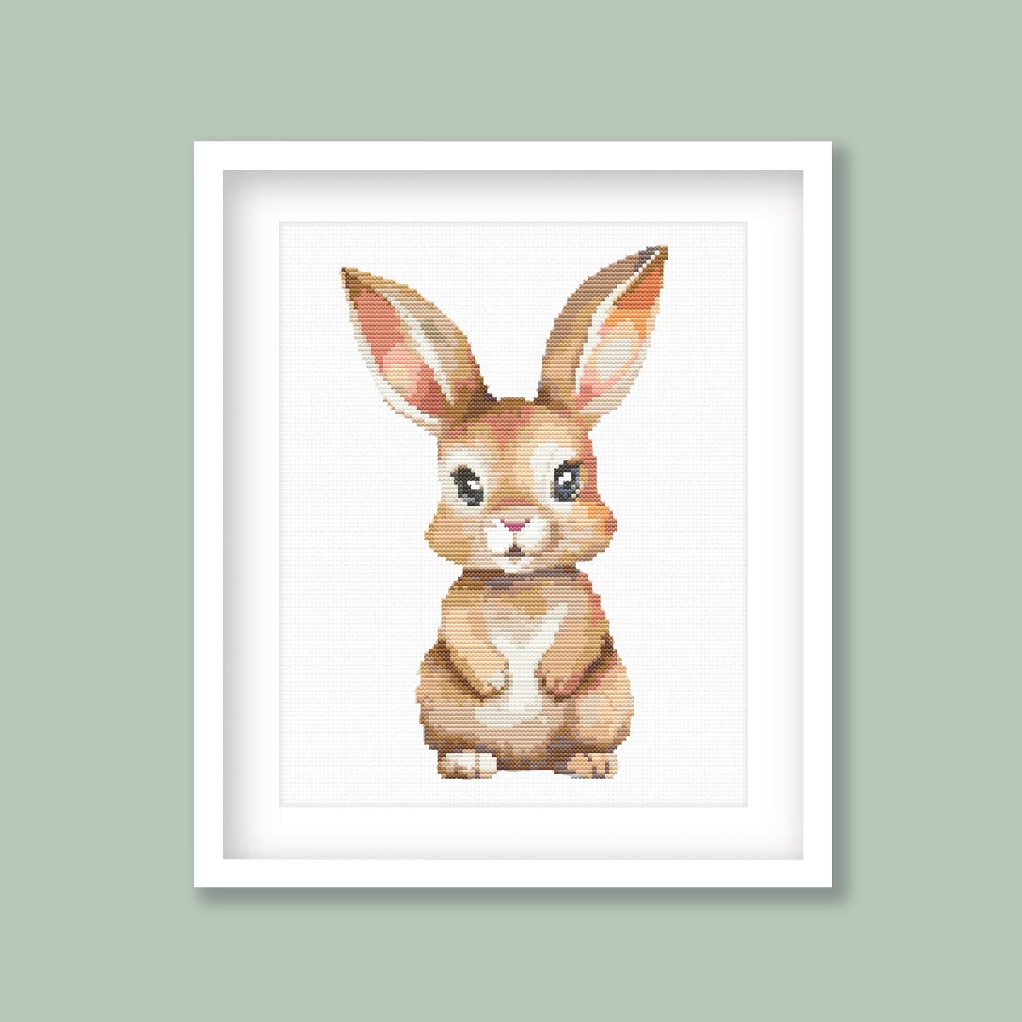 Baby Rabbit Cross Stitch Pattern displayed as framed wall art with a soft bunny design on a sage green background for nursery or kids room decor.