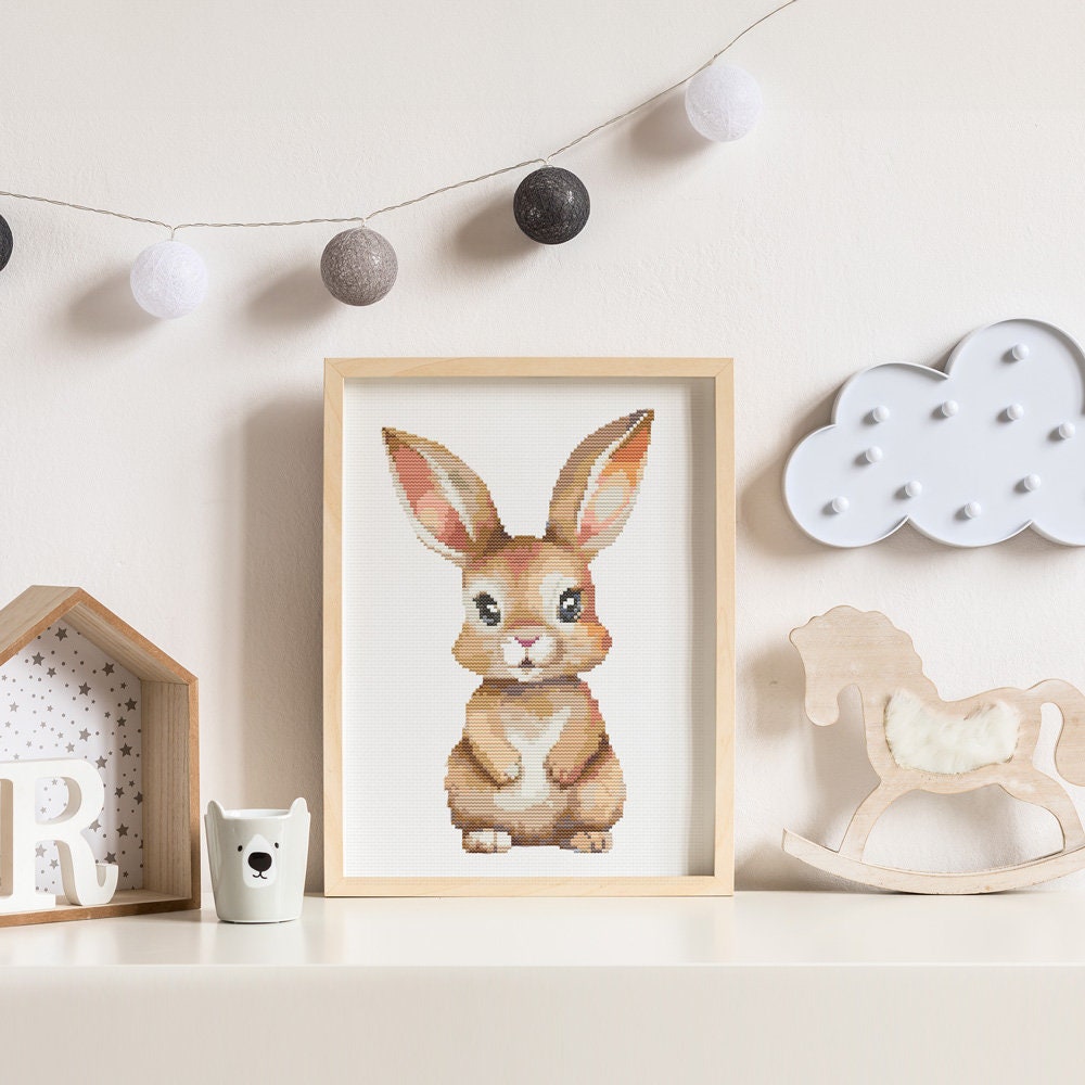 Baby Rabbit Cross Stitch Pattern shown in a nursery room preview with soft decor, framed bunny wall art, and gentle children’s room styling.
