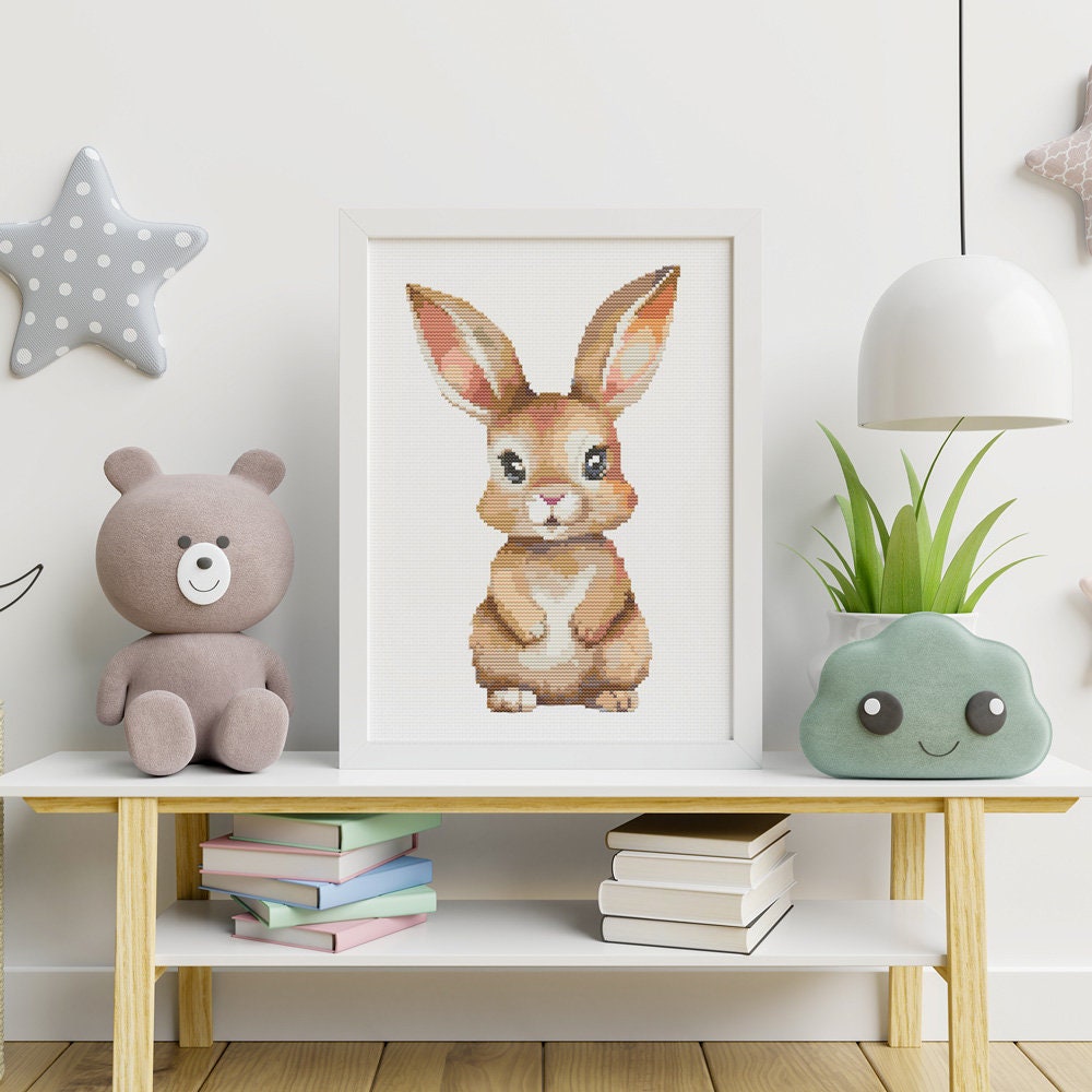 Baby Rabbit Cross Stitch Pattern shown in a children’s room shelf preview with framed bunny artwork, toys, plants, and nursery decor.