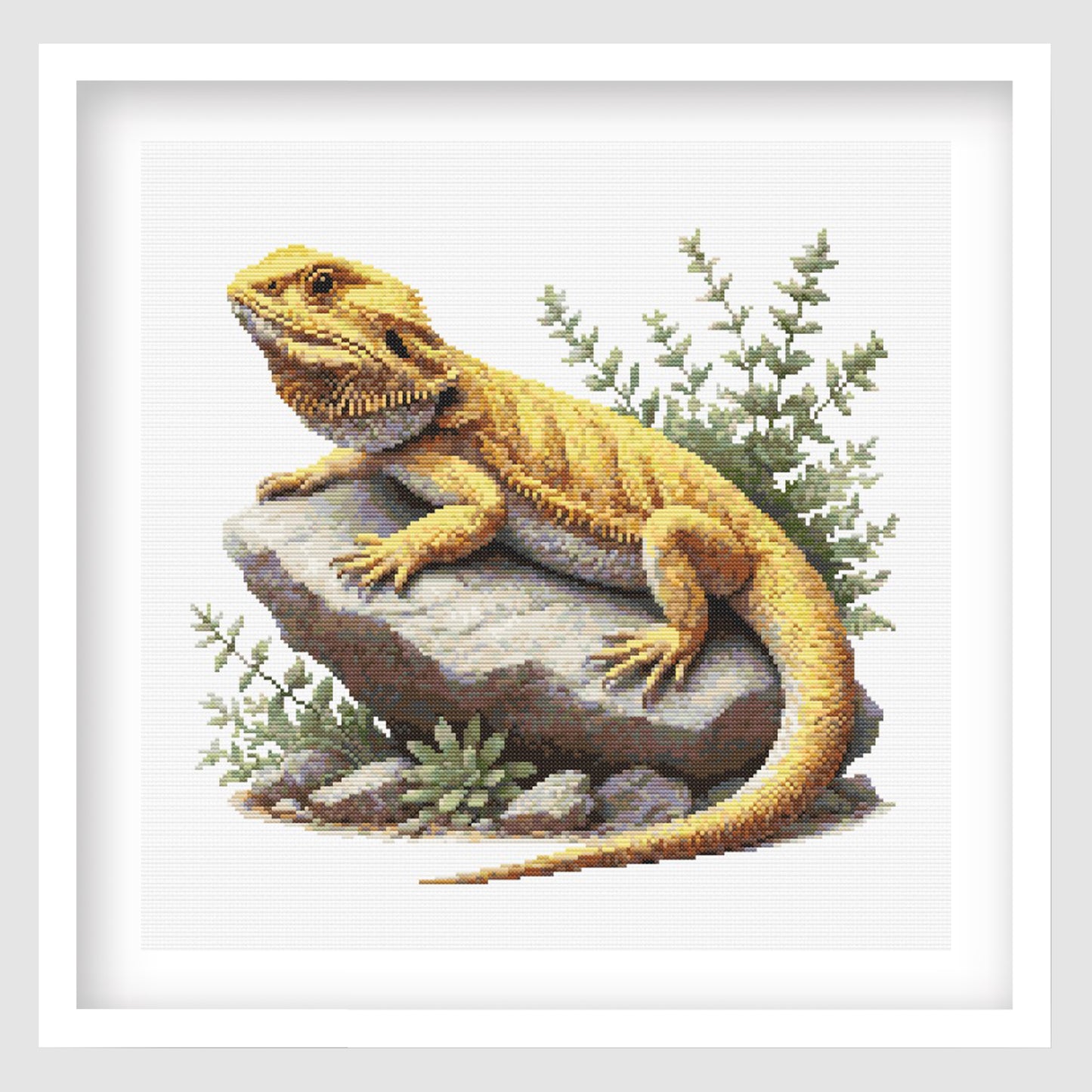 Cross-stitched yellow bearded dragon lizard on a rock with green plants.