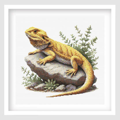 Cross-stitched yellow bearded dragon lizard on a rock with green plants.