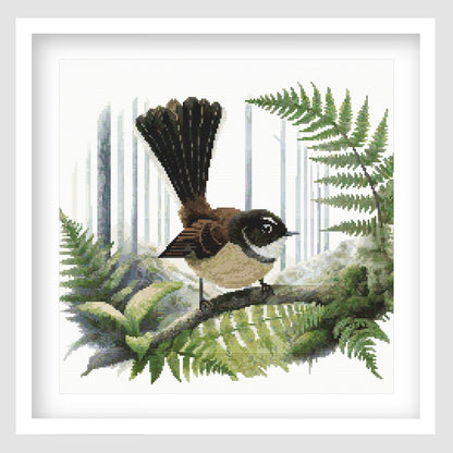 Framed Fantail Pīwakawaka cross stitch featuring a New Zealand fantail perched among native fern fronds.