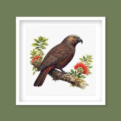 New Zealand Kākā Cross Stitch Pattern displayed in a green frame as native bird wall art with pōhutukawa flowers and natural New Zealand styling.