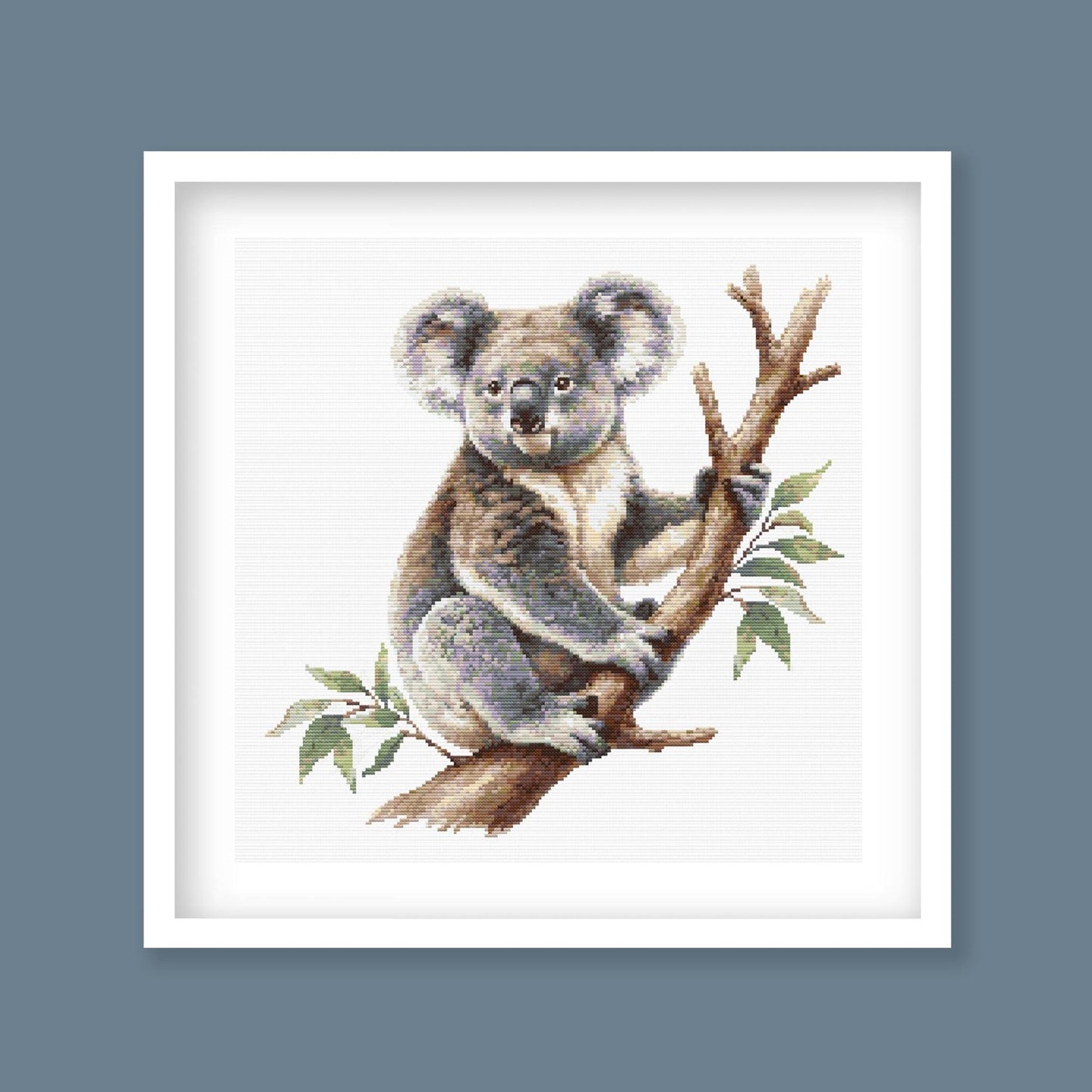 Koala Cross Stitch Pattern displayed in a black frame as Australian wildlife wall art with a koala and eucalyptus branch.