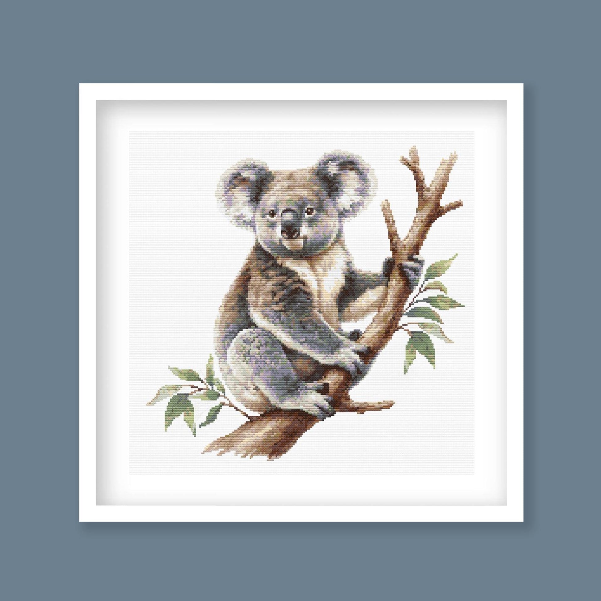 Koala Cross Stitch Pattern displayed in a black frame as Australian wildlife wall art with a koala and eucalyptus branch.