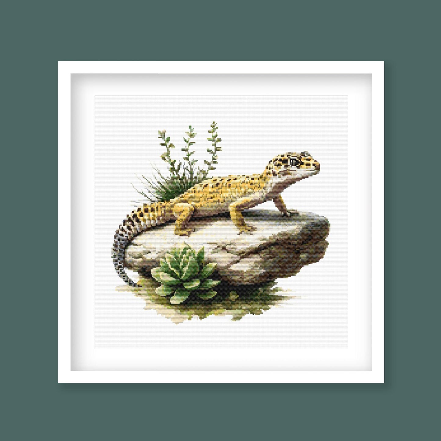 Leopard Gecko Cross Stitch Pattern displayed in a dark frame with a spotted lizard, rock detail, and natural reptile-inspired wall art style.