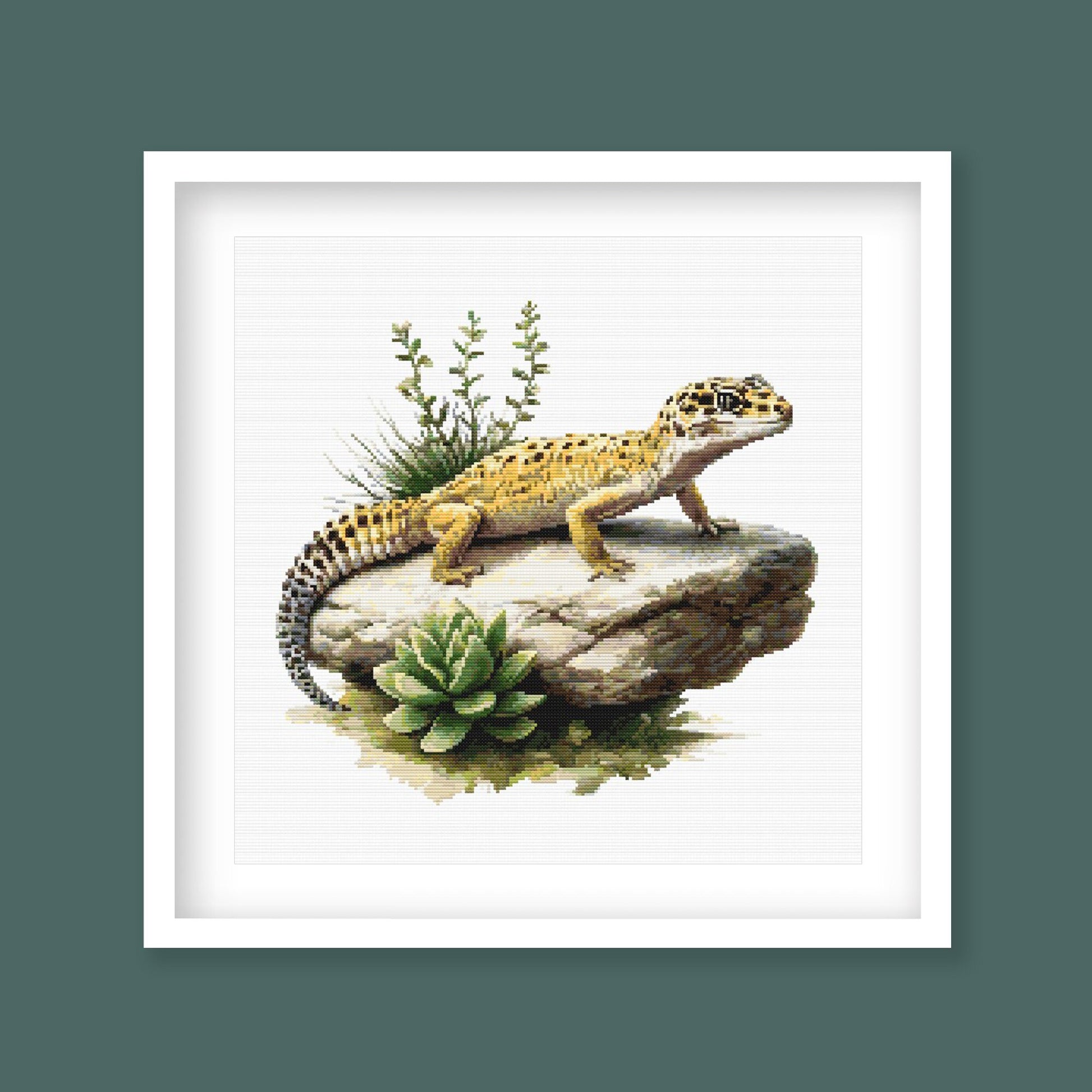 Leopard Gecko Cross Stitch Pattern displayed in a dark frame with a spotted lizard, rock detail, and natural reptile-inspired wall art style.