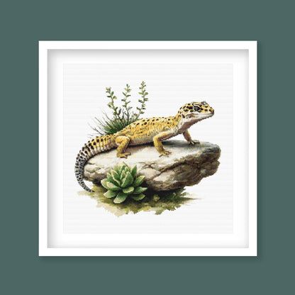 Leopard Gecko Cross Stitch Pattern displayed in a dark frame with a spotted lizard, rock detail, and natural reptile-inspired wall art style.
