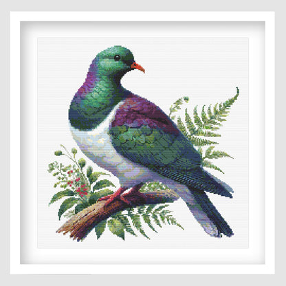 New Zealand Kererū Cross Stitch Pattern displayed as framed wall art with a native wood pigeon, green and purple feathers, fern foliage, and natural bird detail.