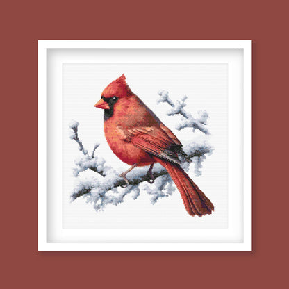 Northern Cardinal Bird Cross Stitch Pattern displayed as framed wall art with a vivid red cardinal perched on snowy branches.