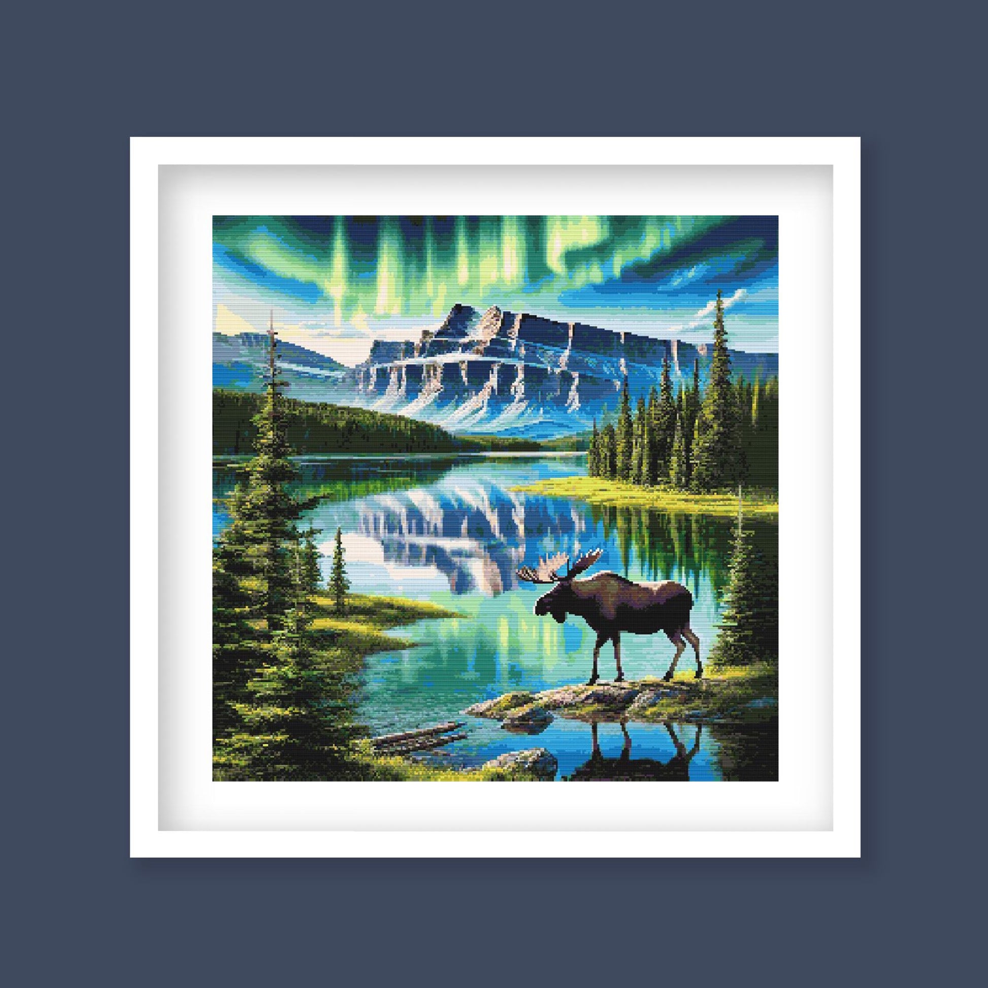 Framed artwork of a moose by a lake with mountains and northern lights in the background.