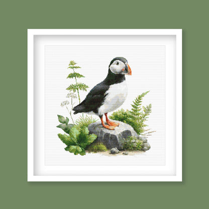 Puffin Cross Stitch Pattern displayed in a green frame as coastal bird wall art with natural foliage and puffin detail.