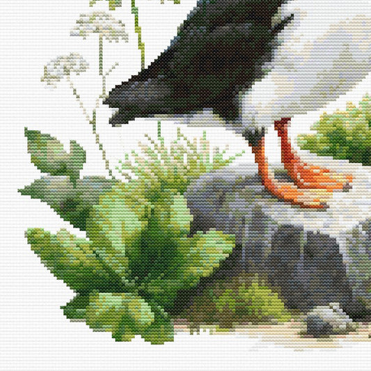 Close-up of Puffin Cross Stitch Pattern showing the puffin’s feet, rocky ground, green foliage, and visible counted cross stitch texture.