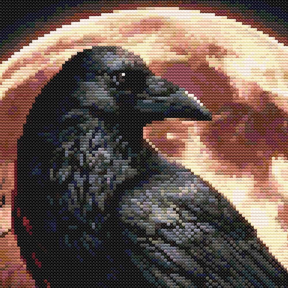 Close-up of a raven cross stitch pattern showing dark feather detail, a glowing blood moon background and dramatic gothic stitching.