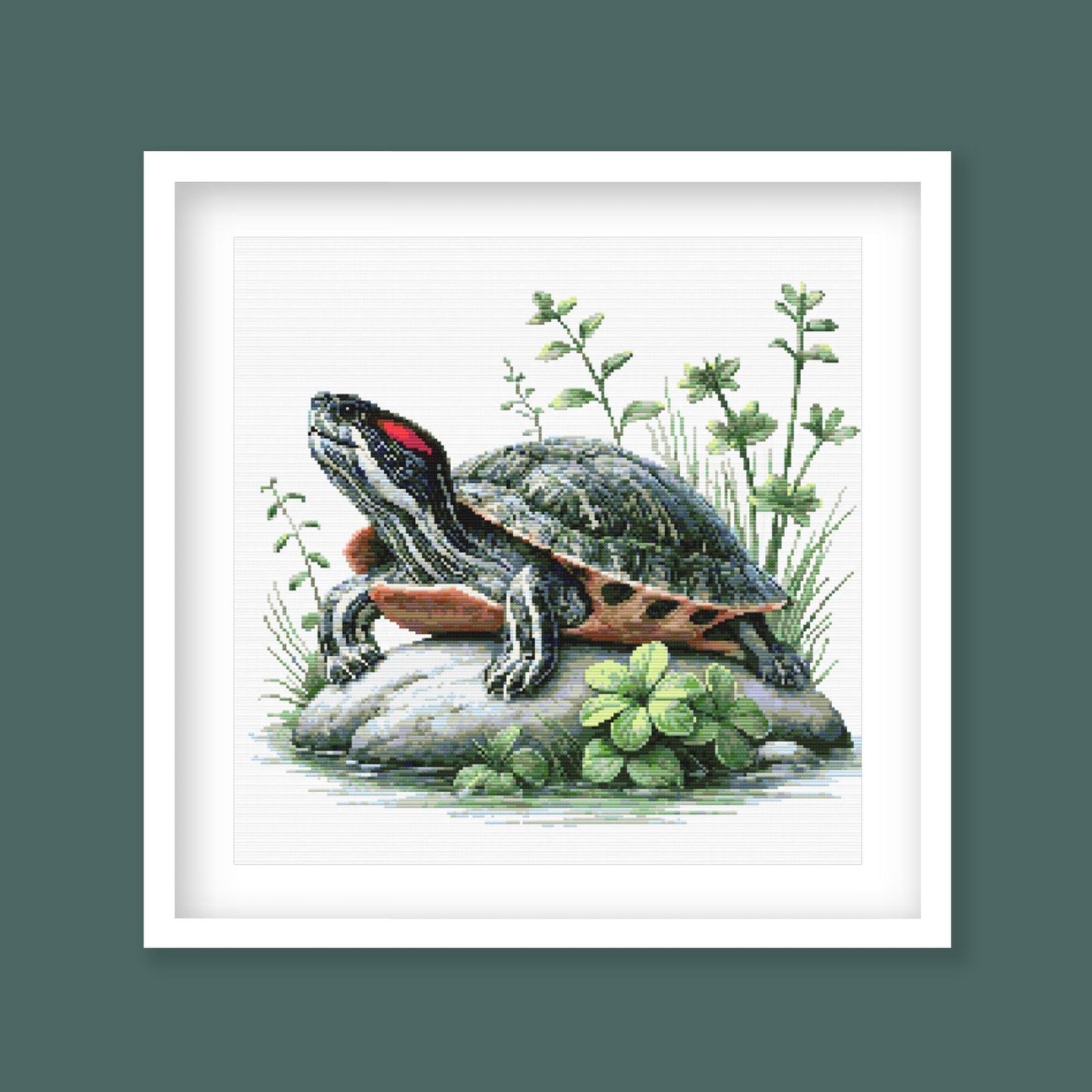 Red-Eared Slider Turtle Cross Stitch Pattern displayed as framed wall art with a detailed turtle, red ear stripe, rock ledge, and natural greenery.