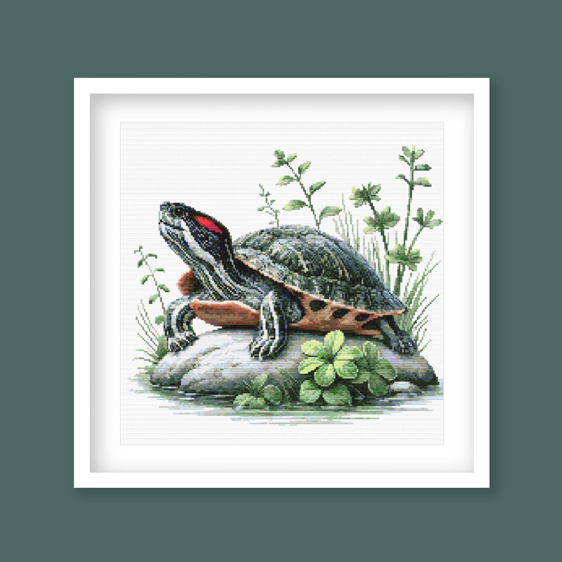 Red-Eared Slider Turtle Cross Stitch Pattern displayed as framed wall art with a detailed turtle, red ear stripe, rock ledge, and natural greenery.