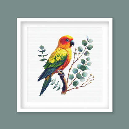 Sun Conure Cross Stitch Pattern displayed as framed wall art with a colourful tropical parrot, orange and yellow feathers, and soft leafy detail.