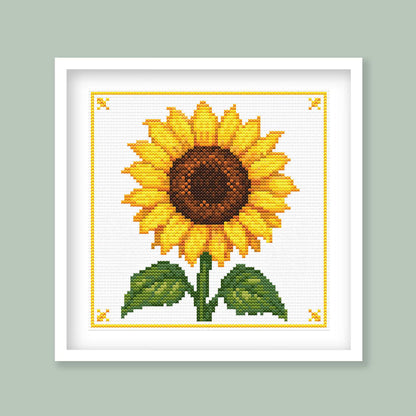 Close-up of a sunflower cross stitch pattern showing yellow petals, a brown centre, green leaves and visible stitched texture.