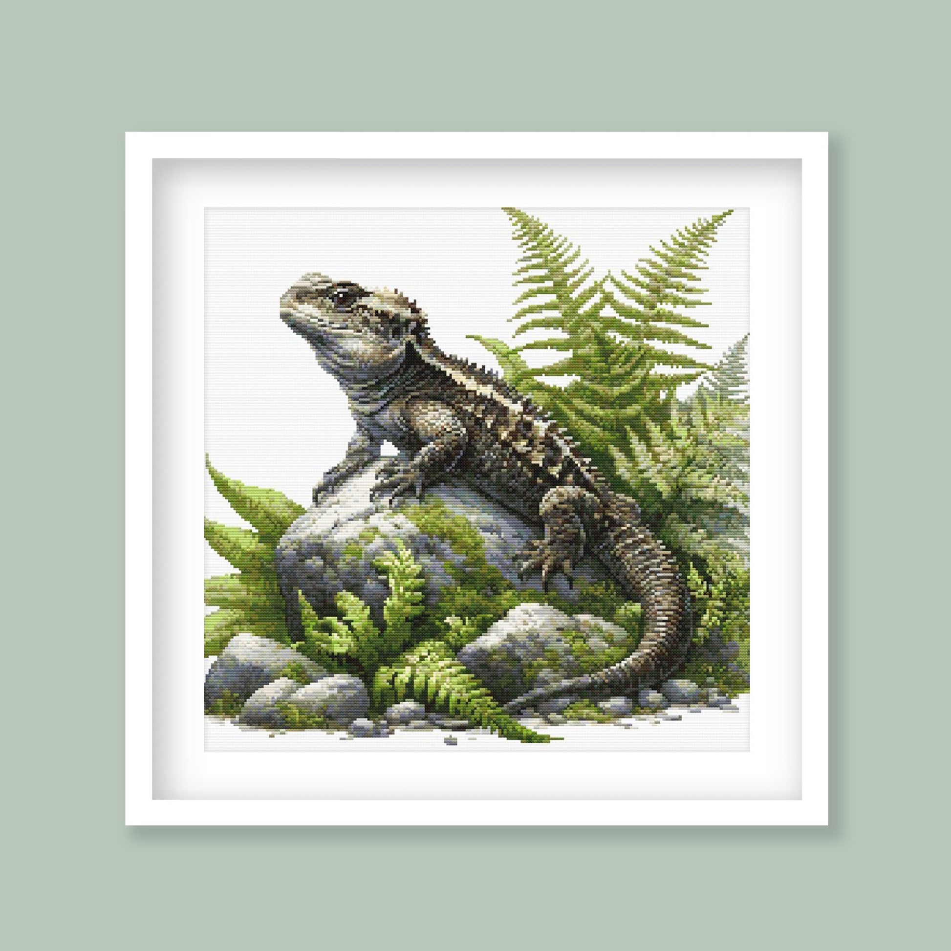 Tuatara Cross Stitch Pattern displayed as framed wall art with a native New Zealand tuatara, fern foliage, mossy rocks, and natural reptile detail.