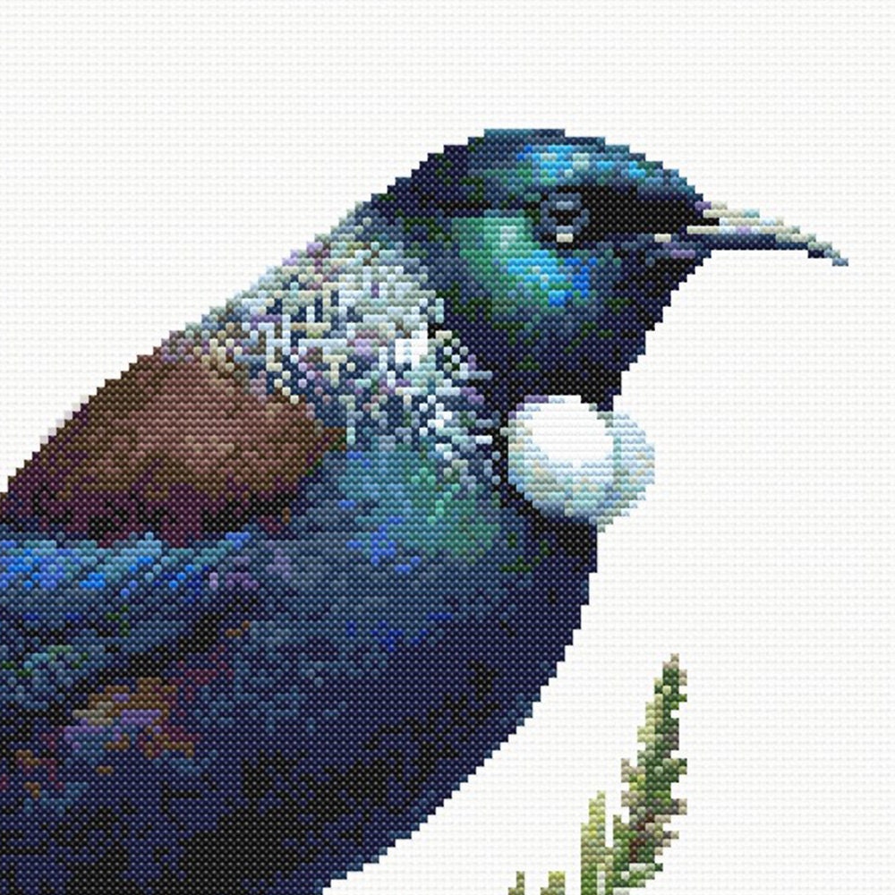 Close-up of New Zealand Tui Cross Stitch Pattern showing glossy dark feathers, blue-green colour, white throat tuft, and visible counted cross stitch texture.