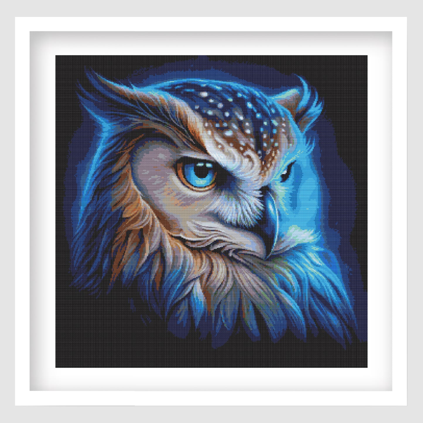 The vibrant owl cross stitch in a white frame on a grey background