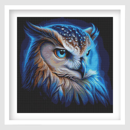 The vibrant owl cross stitch in a white frame on a grey background
