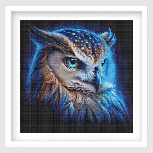 The vibrant owl cross stitch in a white frame on a grey background